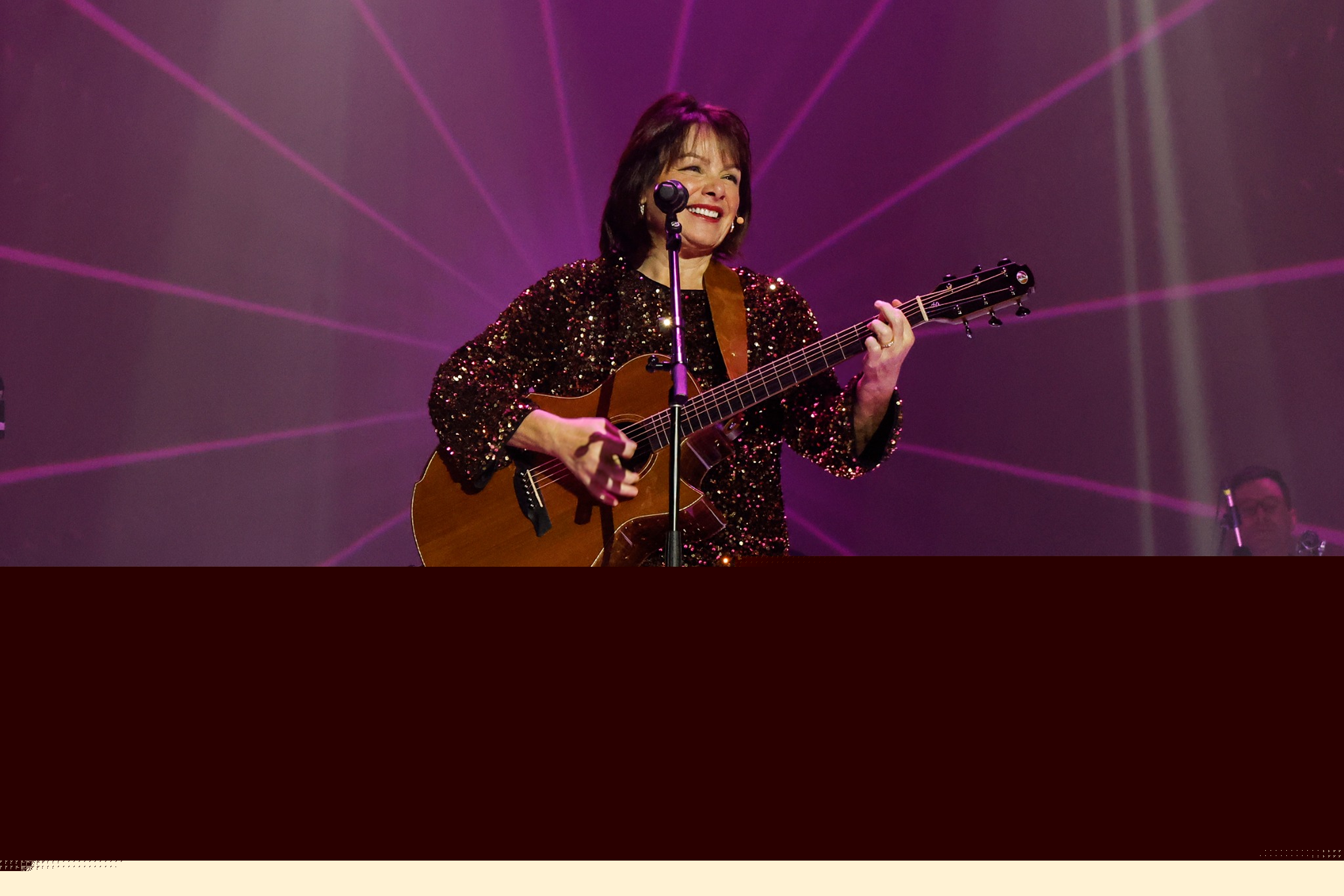 Sheila Williams smiling on stage with her guitar